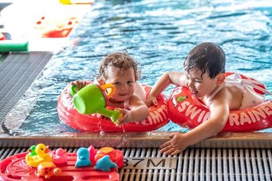 Zwei Kleinkinder planschen fröhlich mit Schwimmringen und Wasserspielzeug im Poolbereich des Familienhotels Ramsi in Kärnten