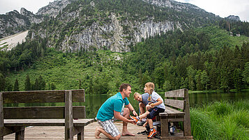 Mutter und Vater sitzen gemeinsam mit ihrer Tochter auf einer Bank am Frillensee in Bayern.