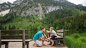 Mutter und Vater sitzen gemeinsam mit ihrer Tochter auf einer Bank am Frillensee in Bayern.