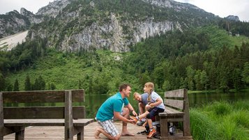 Mutter und Vater sitzen gemeinsam mit ihrer Tochter auf einer Bank am Frillensee in Bayern.