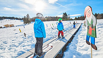 Kinder stehen auf den Skiern auf einem Zauberteppich in der Skischule.