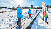 Kinder stehen auf den Skiern auf einem Zauberteppich in der Skischule.