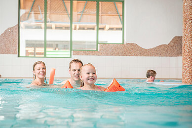 Eltern bringen ihrem Sohn im Schwimmbad des Familienhotels Landgut Furtherwirt das Schwimmen bei.