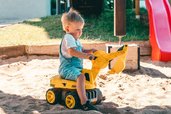 Kleines Kind spielt konzentriert mit einem gelben Bagger im Sandkasten des Familienhotels Friedrichshof.