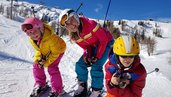 Fröhliche Kinder gemeinsam mit einer Skilehrerin beim Skifahren in den Kärntner Bergen