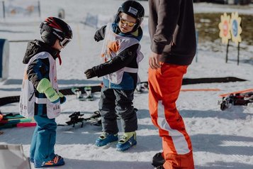 Kinder stehen beim Skikurs des Familienhotel Mia Alpina in Tirol mit Skiern im Schnee und werden betreut.