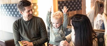 Familie sitzt mit Kleinkind im Hotel und schaut ein Buch an