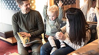 Familie sitzt mit Kleinkind im Hotel und schaut ein Buch an