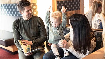 Familie sitzt mit Kleinkind im Hotel und schaut ein Buch an