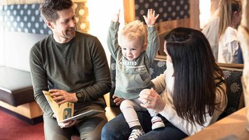 Familie sitzt mit Kleinkind im Hotel und schaut ein Buch an