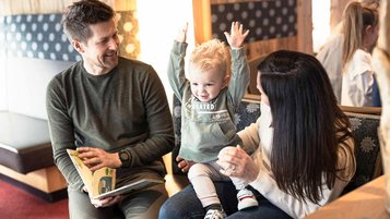 Familie sitzt mit Kleinkind im Hotel und schaut ein Buch an