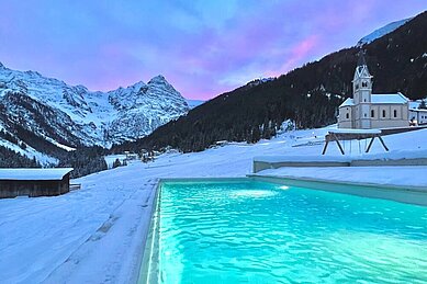 Abendlicher Blick über den Aussenpool im Familienhotel Bella Vista in Südtirol in die Dolomiten. 