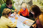 Eltern spielen mit ihren beiden Kindern ein digitales Brettspiel im Happy-Club des Familienhotels Sailer in Tirol.