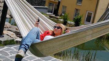 Ein Teenager Mädchen liegt in einer Hängematte im Hotel Engel im Schwarzwald und schaut auf ihr Handy