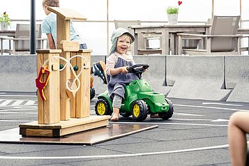 Ein kleines Kind fährt auf einem Bobbycar und lacht im Familienhotel Allgäuer Berghof im Allgäu