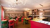 Bunte und familienfreundliche Restaurantbar im Familienhotel Deichkrone an der Nordsee, mit lebhaft roten und grünen Stühlen und einem gemütlichen Ambiente, beleuchtet durch stilvolle Deckenleuchten.