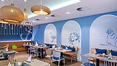Buntes und familienfreundliches Restaurant im Familienhotel Deichkrone an der Nordsee, mit lebhaft roten und grünen Stühlen und einem gemütlichen Ambiente, beleuchtet durch stilvolle Deckenleuchten.