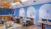 Buntes und familienfreundliches Restaurant im Familienhotel Deichkrone an der Nordsee, mit lebhaft roten und grünen Stühlen und einem gemütlichen Ambiente, beleuchtet durch stilvolle Deckenleuchten.