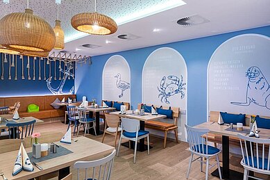 Buntes und familienfreundliches Restaurant im Familienhotel Deichkrone an der Nordsee, mit lebhaft roten und grünen Stühlen und einem gemütlichen Ambiente, beleuchtet durch stilvolle Deckenleuchten.