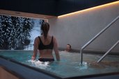 Paar entspannt im warmen Rooftop-Pool mit Blick auf die verschneite Winterlandschaft im Familienhotel Habachklause.