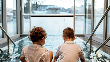Zwei Kleinkinder sitzen am Beckenrand im Wellnessbereich des Post Family Resorts im Salzburger Land.
