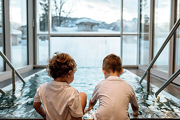 Zwei Kleinkinder sitzen am Beckenrand im Wellnessbereich des Post Family Resorts im Salzburger Land.