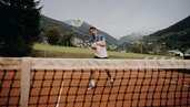 Ein Vater spielt auf dem Tennisplatz des Hotel Sonngastein im Salzburger Land vor Bergkulisse Tennis.