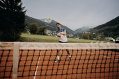 Ein Vater spielt auf dem Tennisplatz des Hotel Sonngastein im Salzburger Land vor Bergkulisse Tennis.