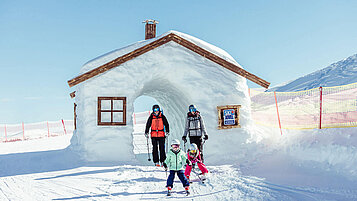 Dreiköpfige Familie fährt auf den Skiern durch einer aus Schnee gebauten Hütte.