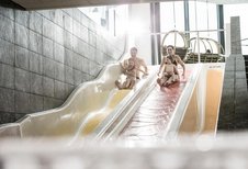 Eltern rutschen mit ihren beiden Kindern die Wasserrutschen im Familienhotel Allgäuer Berghof hinunter.