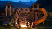 Kinder sitzen in einem Sitzkreis um ein Lagerfeuer mit einem Betreuer im Familienhotel Alphotel Tyrol Wellness & Family Resort in Südtirol.