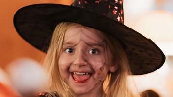 Ein zu Halloween als Hexe verkleidetes Mädchen lacht in die Kamera