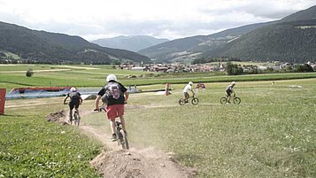 Teens fahren im Familienhotel Alpenhof Dolomit Family einen Berg mit Fahrrad runter. 