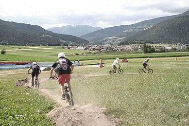 Teens fahren im Familienhotel Alpenhof Dolomit Family einen Berg mit Fahrrad runter. 