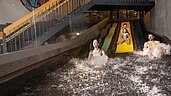 Familie mit zwei Kindern rutscht auf den Wasserrutschen im Schwimmbad des Familienhotels Alpenhotel Kindl ins Becken.