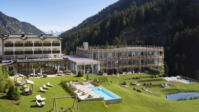 Außenansicht des Familienhotels Bella Vista mit modernem Neubau, Außenpool, Spielplatz und herrlicher Bergkulisse.