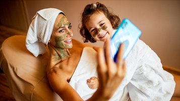 Eine Mutter mit ihrem Kind bei einer Gesichtsbehandlung und machen ein Selfie mit dem Handy im Familienhotel Das Bayrischzell in Oberbayern