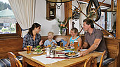 Eine Familie bei Mittagessen im Spa- & Familien-Resort Krone im Allgäu. Auf dem Tisch stehen leckere traditionelle Käsespätzle, frischer Salat und Pommes für die beiden Kinder.