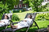 Zwei Jugendliche entspannen in Bademänteln auf Sonnenliegen im Garten des Familienhotel Sonne Bezau.