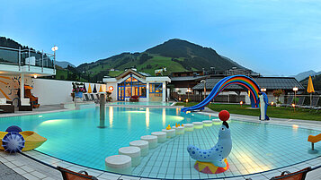 Pool mit Kinderrutsche und anderen Spielmöglichkeiten mit Ausblick auf die Berge im Wellness- & Familienhotel Egger in Saalbach Hinterglemm.