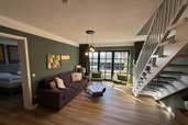 Wohnbereich mit gemütlichem Sofa, Treppe zur Galerie und direktem Zugang zur Terrasse im Familienhotel Gut Landegge
