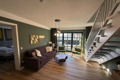 Wohnbereich mit gemütlichem Sofa, Treppe zur Galerie und direktem Zugang zur Terrasse im Familienhotel Gut Landegge