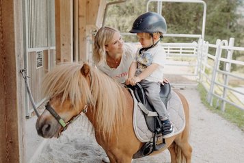 Kleiner Junge sitzt auf einem Pony im Reitstall des Habachklause Familien Bauernhof Resorts im Salzburger Land.