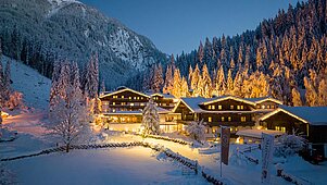 Das Hotel Habachklause im Salzburger Land erstrahlt bei Nacht in festlicher Beleuchtung, eingebettet in eine idyllische, schneebedeckte Landschaft mit dichten Tannen und einem beeindruckenden Berg im Hintergrund.