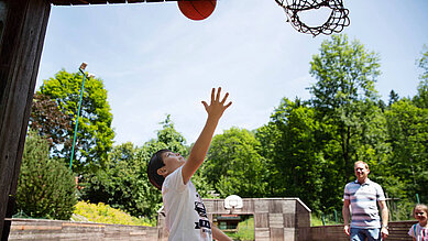 Jugendlicher Junge spielt mit seinem Vater Basketball auf dem Basketballplatz des Kinderhotels Bruckwirt.