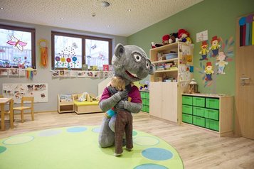 Das Kind umarmt in der Kinderbetreuung das Maskottchen des Familienhotels Das Bayrischzell in Bayern.