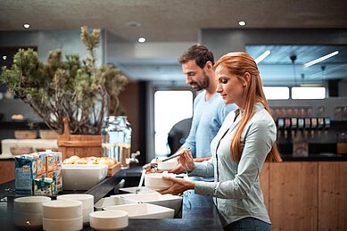 Eltern bedienen sich am reichhaltigen Frühstücksbuffet des Familienhotels Family Home Alpenhof.