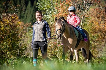 Kind reitet gemeinsam mit einer Reitlehrerin beim Reitunterricht durch die Natur rund um das Familienhotel Oberkarteis.