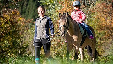 Kind reitet gemeinsam mit einer Reitlehrerin beim Reitunterricht durch die Natur rund um das Familienhotel Oberkarteis.