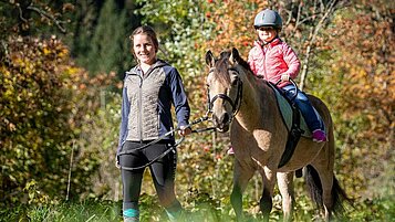 Kind reitet gemeinsam mit einer Reitlehrerin beim Reitunterricht durch die Natur rund um das Familienhotel Oberkarteis.